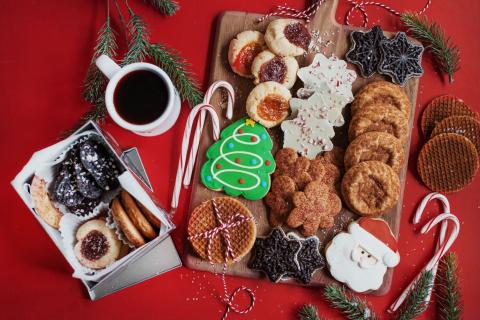 A variety of christmas cookies on a platter with candy canes and coffee.